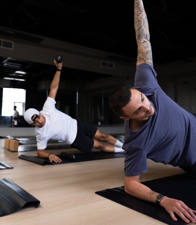 Members in side plank with light dumbbells during a heated sculpt class at Forma