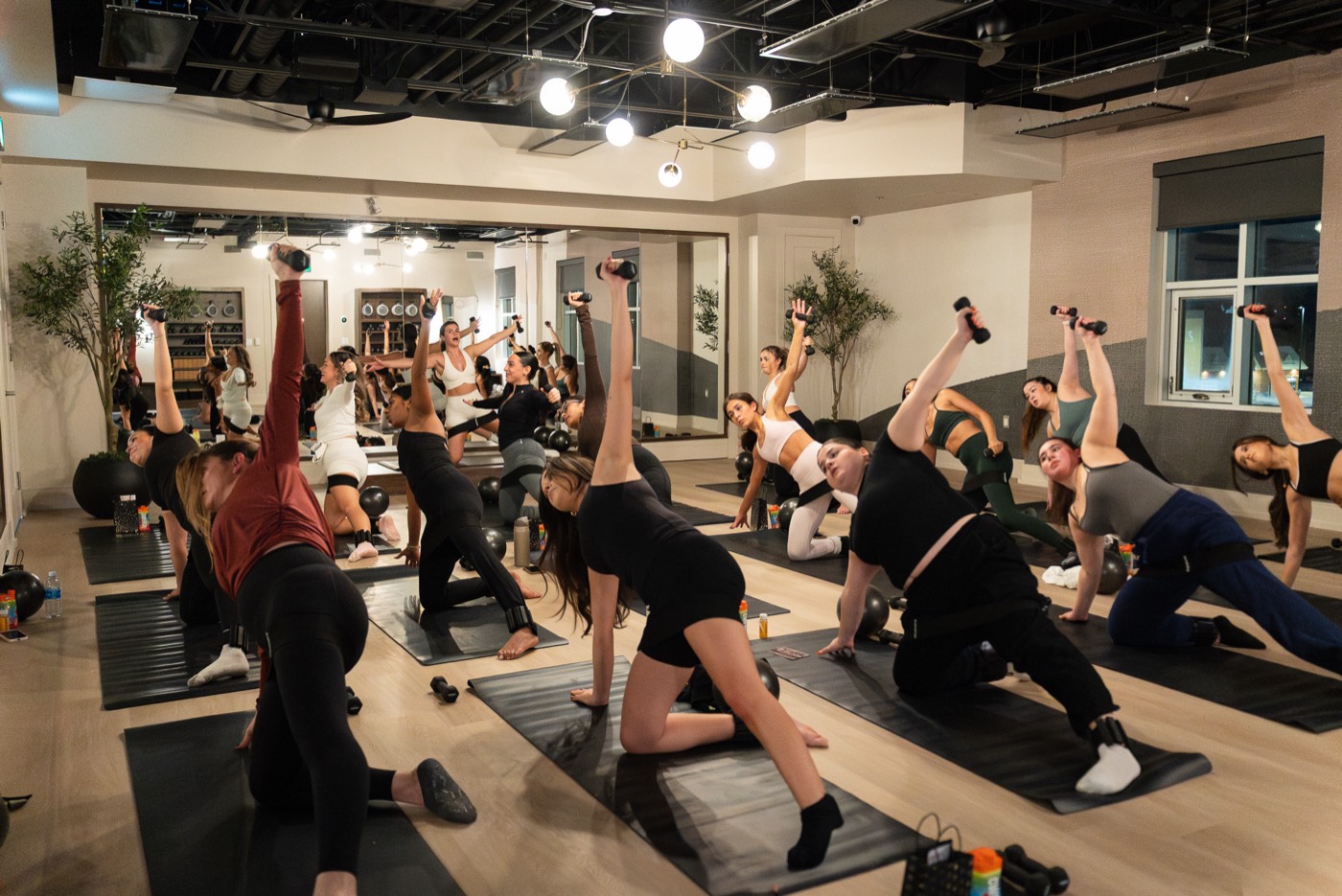A full heated mat class holding kneeling side bends with dumbbells during Power Sculpt at Forma