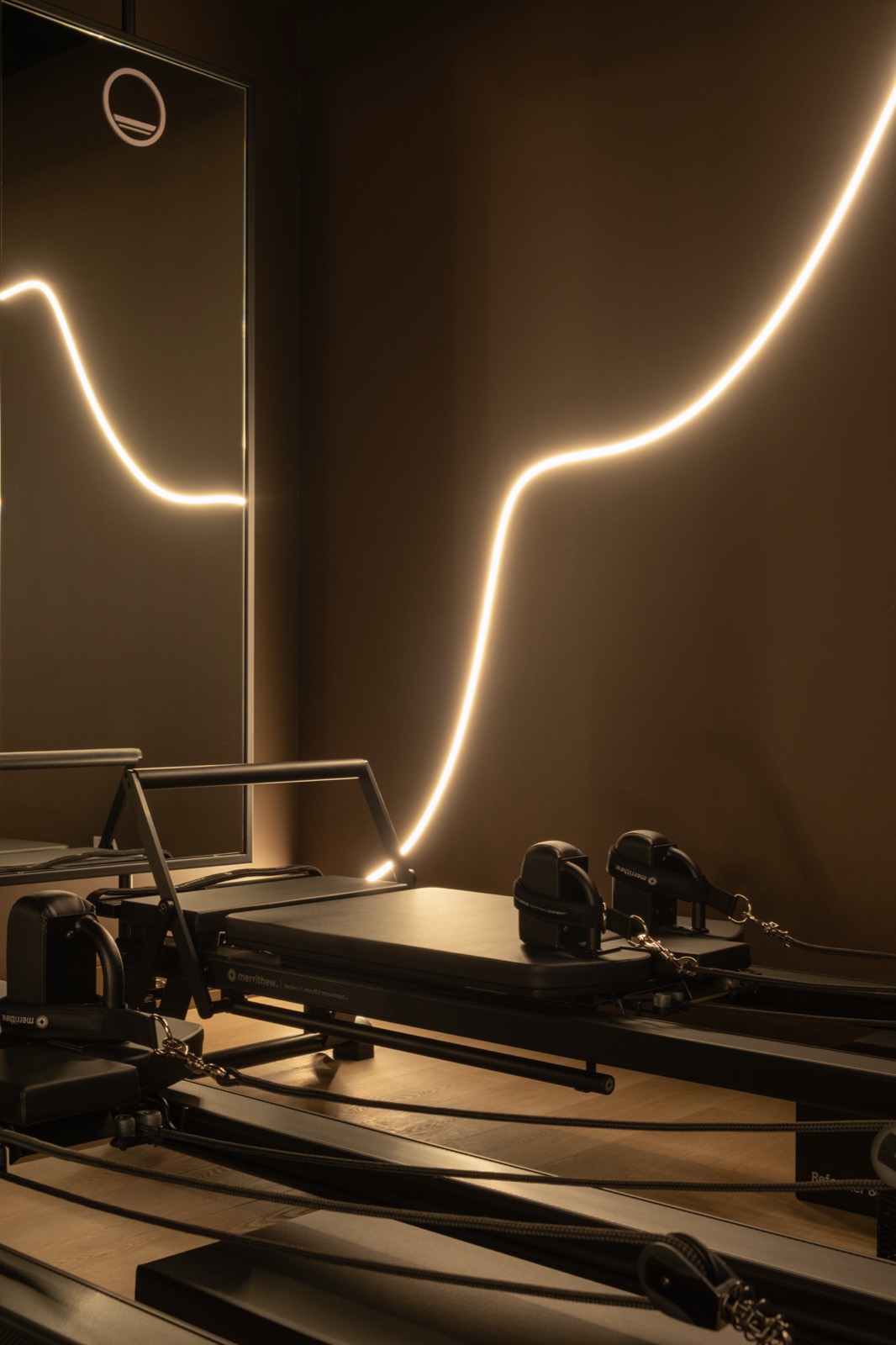 Reformer carriage in the Forma studio beneath a sculpted neon light and mirror