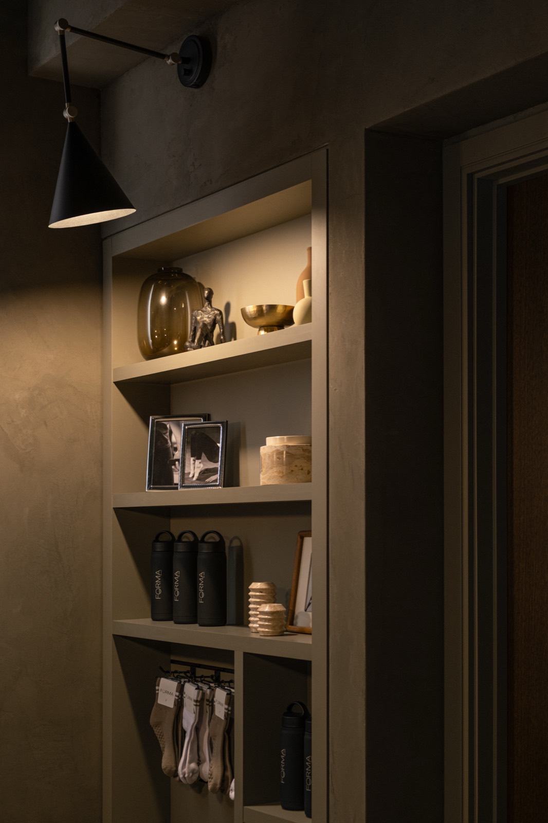 Forma retail shelf lit by a wall lamp with bottles, socks, and framed prints