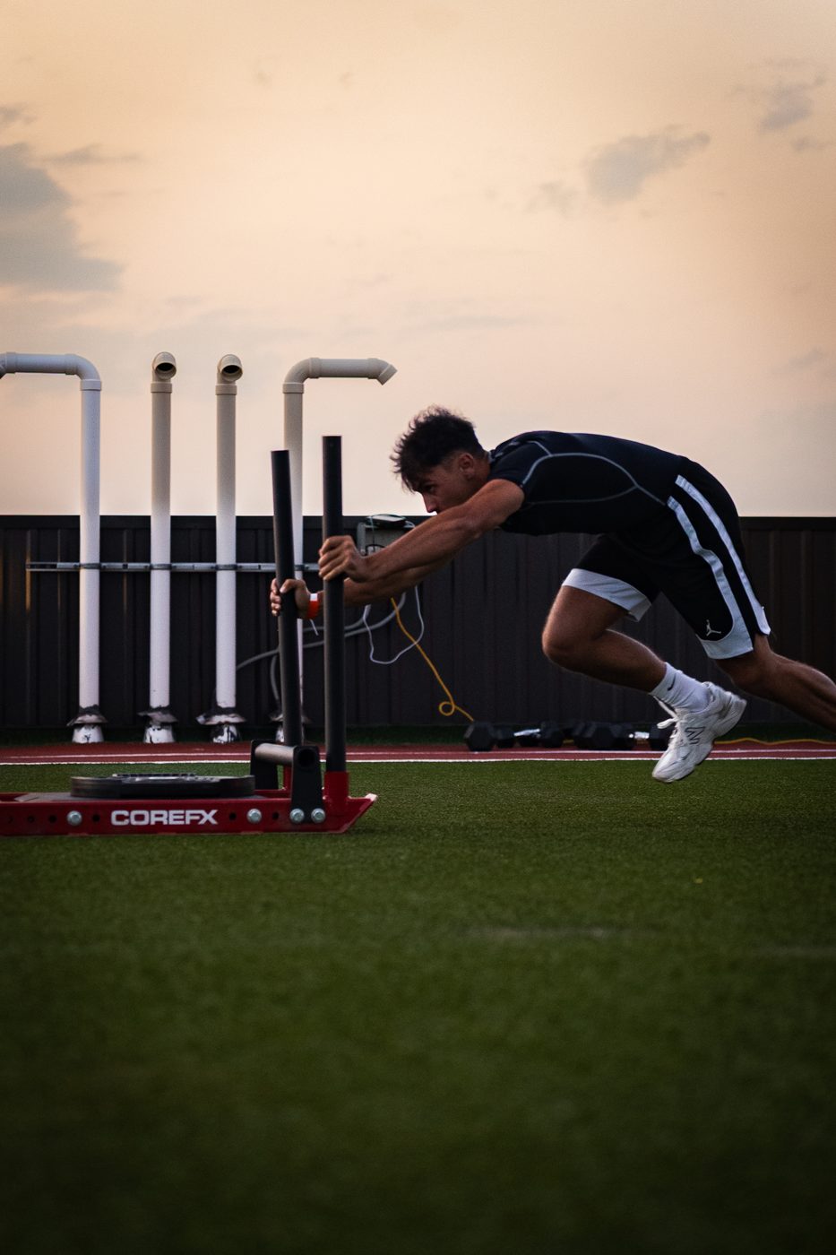 Athlete pushing a training sled on the ACE rooftop turf at sunset